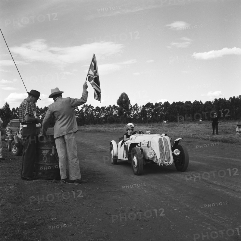 On your marks. A man holds up a union jack flag for car number 101, an Anglia Special, at the start of race eleven at the Eldoret race meeting. Eldoret, Kenya, 27 December 1954. Eldoret, Rift Valley, Kenya, Eastern Africa, Africa.