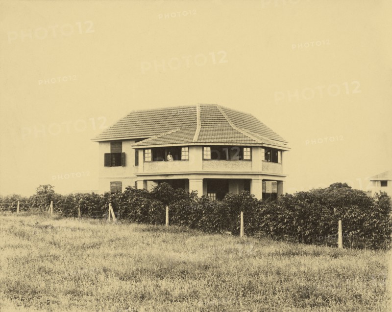 Railway house and garden. A railway house, property of the Kenya & Uganda Railways, used to accommodate senior British employees. At the time of the photograph it was home to Parlane Macfarlane (the man on the balcony), an engineer with KUR. Mombasa, Kenya, circa 1930. Mombasa, Coast, Kenya, Eastern Africa, Africa.
