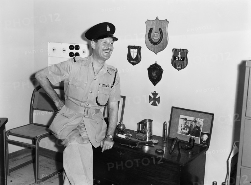 Jasper Maskelyne and his trophies. Jasper Maskelyne as a Kenyan Police officer proudly poses next to a selection of trophies and memorabilia. The shoulder epaulettes on his uniform read 'KENYA POLICE' and his shirt displays numerous military medals. Kenya, 24 February 1953. Kenya, Eastern Africa, Africa.