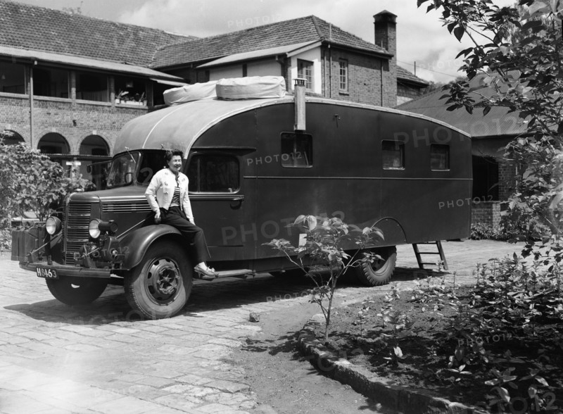 The Price's caravan. A woman sits on the wheel-arch of an old-fashioned caravan in the driveway to large house. Kenya, 12 May 1953. Kenya, Eastern Africa, Africa.