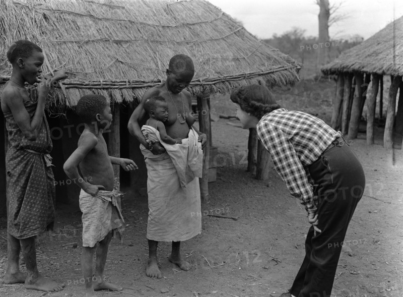Mrs Price meets a baby. Mrs Price leans in to communicate with a baby sitting on its mother's hip. Mozambique, September 1953. Mozambique, Southern Africa, Africa.