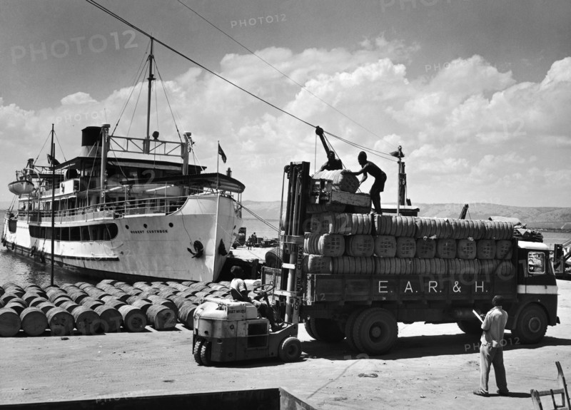 Unloading cotton bales at Lake Albert. A publicity photograph from the East African Railways and Harbours Administration (EAR&H) showing workers unloading bales of cotton from an EAR&H freight truck onto a wharf at Lake Albert. Western Division, Uganda, circa 1955., West (Uganda), Uganda, Eastern Africa, Africa.