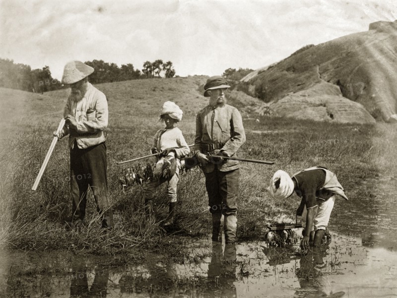Snipe hunting. Two British snipe hunters stand, shotguns in hand, as their young Indian assistants gather downed birds and hang them onto wooden racks. India, circa 1860. India, Southern Asia, Asia.