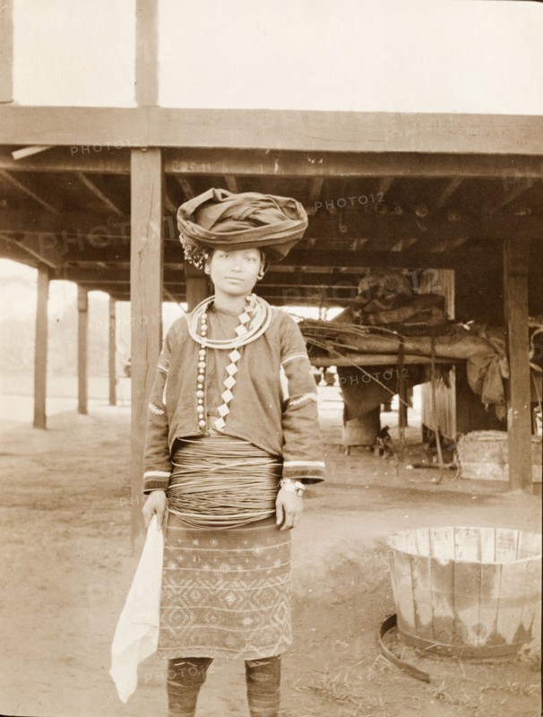 Kachin woman in traditional dress. Portrait of a Kachin woman dressed in traditional costume. She wears multiple hoops that encircle her waist and neck, and a cloth scarf wrapped around her head. Kachin State, Burma (Myanmar), circa 1910., Kachin, Burma (Myanmar), South East Asia, Asia.