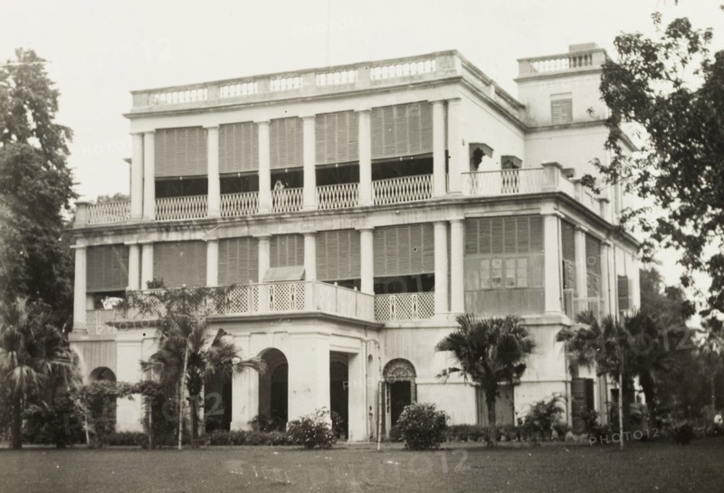 facade of a colonial-style building. The colonnaded facade of a two-storey, colonial building, featuring a projecting front porch, and a square tower at the rear. Probably India, circa 1950. India, Southern Asia, Asia.