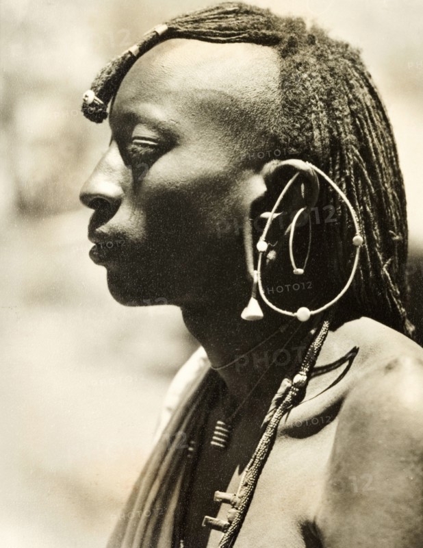 African man with a distinctive earring. Profile shot of the head and shoulders of a young African man. Naked from the waist up, he wears a plaited hairstyle, necklaces and a large, distinctive earring. Probably Northern Rhodesia (Zambia), circa 1950. Zambia, Southern Africa, Africa.