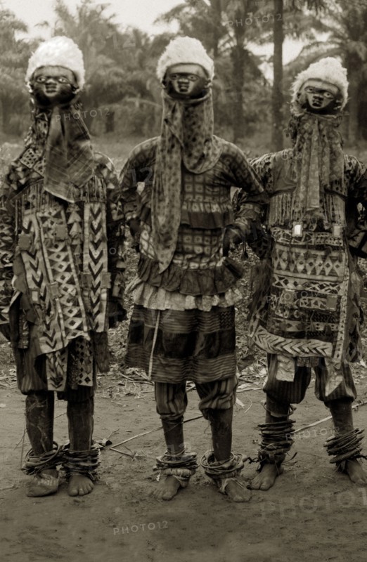 Juju practitioners. Three juju dancers in costume wear wooden masks on top of their heads, ornate patterned clothing and anklets. Possibly Badagry, Nigeria, circa 1925. Nigeria, Western Africa, Africa.