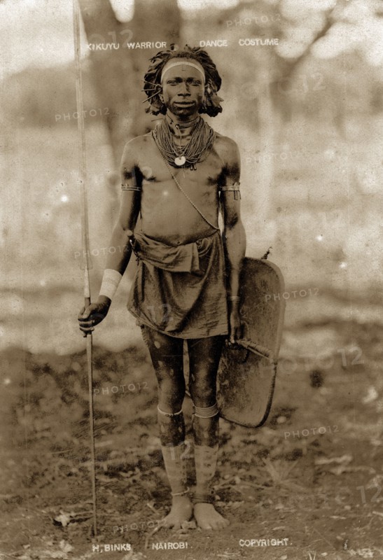 Kikuyu warrior. Full-length portrait of a Kikuyu man wearing neck ornaments and a waist cloth and holding a spear and shield. Kenya, circa 1930. Kenya, Eastern Africa, Africa.