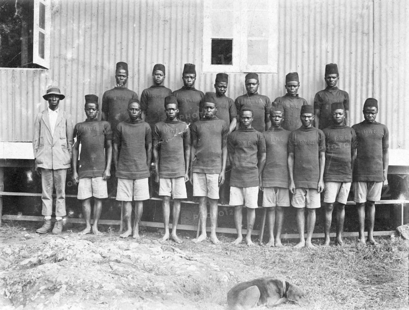 Employees of the Public Works Department. Group portrait of 17 African employees at the Public Works Department. All but one of the line-up wears a uniform consisting of shorts and a military-style jumper or sweater displaying the initials 'PWD' on the chest. British East Africa (Kenya), 1912., Nairobi Area, Kenya, Eastern Africa, Africa.