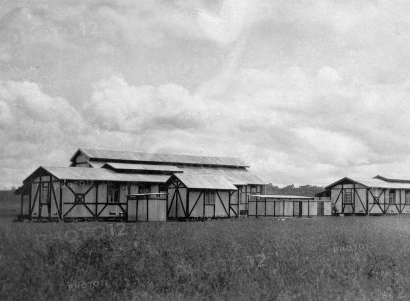 Apprentices' quarters. Several light timber-framed buildings with tin roofs are clustered together in a field, providing housing for apprentices in the Kenyan Public Works Department. They were erected under the supervision of Charles Bungey, a training officer with the PWD. Nakuru, Kenya, 1923. Nakuru, Rift Valley, Kenya, Eastern Africa, Africa.