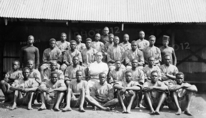 Apprentices in the Public Works Department. Group portrait showing Charles Bungey, a training officer in the Kenyan Public Works Department, seated in the centre of 30 young African men. Nakuru, Kenya, circa 1923. Nakuru, Rift Valley, Kenya, Eastern Africa, Africa.