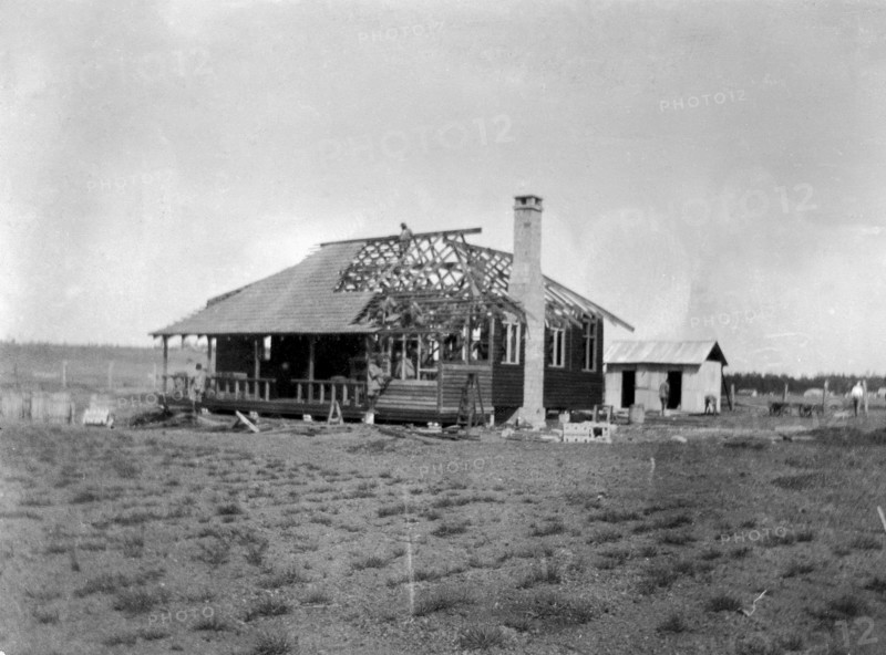 Building a house. This is the first in a series of four photographs showing the rapid erection of a timber-framed European-style house. The photograph shows the house from the front, with a stone chimney rising up the side. The house was built for Charles Bungey, a training officer with the Kenyan Public Works Department, by the local apprentices of his department. Nakuru, Kenya, March 1922. Nakuru, Rift Valley, Kenya, Eastern Africa, Africa.