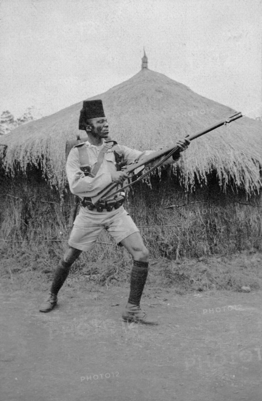 Askari from Second King's African Rifles. An African askari (soldier) poses with his gun in front of a grass-roofed dwelling. A caption identifies him as a Guard Sergeant Major of the Second Battalion of the King's African Rifles. British East Africa (Kenya), circa 1916. Kenya, Eastern Africa, Africa.