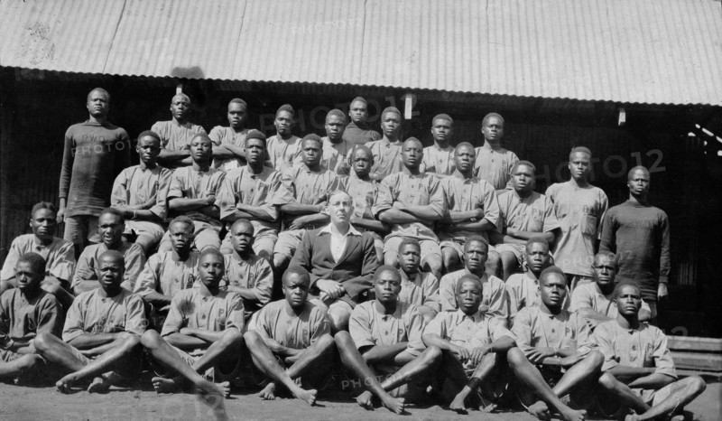 Apprentices in the Public Works Department. Group portrait showing Charles Bungey, a training officer in the Kenyan Public Works Department, seated in the centre of over thirty young African men. Kenya, 1924. Kenya, Eastern Africa, Africa.