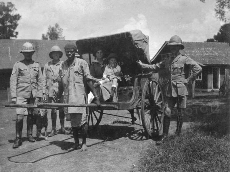 Europeans in a rickshaw. An African rickshaw puller poses with his passengers, a European woman and child, between three European army officers. Nairobi, British East Africa (Kenya), 21 April 1916. Nairobi, Nairobi Area, Kenya, Eastern Africa, Africa.