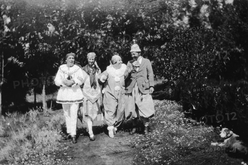 Christmas fancy dress. Four Europeans stroll arm-in-arm down a garden path wearing fancy dress. Charles Bungey (far left) and his wife (third left) wear clown's costumes. Machakos, Kenya, December 1926. Machakos, East (Kenya), Kenya, Eastern Africa, Africa.