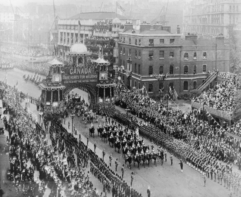 Coronation celebrations for Edward VII. The royal carriage proceeded by mounted soldiers passes through the arch of an elaborately decorated float that reads 'Canada, Free Homes for Millions, God Bless the Royal Family' at Edward VII's coronation procession. The parade is flanked by military men in uniform and an enormous crowd of onlookers cheer and wave as it passes. London, England, 9 August 1902. London, London, City of, England (United Kingdom), Western Europe, Europe .