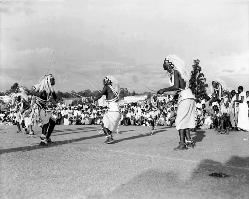 Watusi dancers at the Kampala Trade Show. Male Watusi dancers wearing traditional costume and elaborate feathered headdresses, perform a dance with sticks for a crowd of African spectators at the Kampala trade show. Kampala, Uganda, 15-18 December 1955. Kampala, Central (Uganda), Uganda, Eastern Africa, Africa.