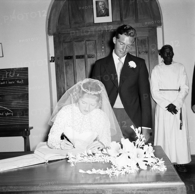 June Watkin signs the register. Bride June Watkin signs the marriage register in the presence of her newlywed husband at their wedding ceremony. An African priest can be seen in the background. Kenya, 5 November 1955. Kenya, Eastern Africa, Africa.