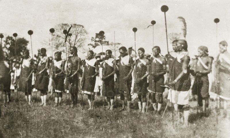 African dancers in costume. A group of African men dressed in ceremonial costume hold sticks as they prepare to perform a traditional dance. Nairobi, Kenya, 12-17 January 1924. Nairobi, Nairobi Area, Kenya, Eastern Africa, Africa.