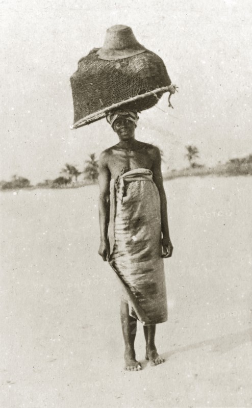 East African fisherwoman. An east African fisherwoman balances a large basket and fishing net on her head, topped off with a gentlemen's hat. Eastern Africa, 12-17 January 1924., Eastern Africa, Africa.