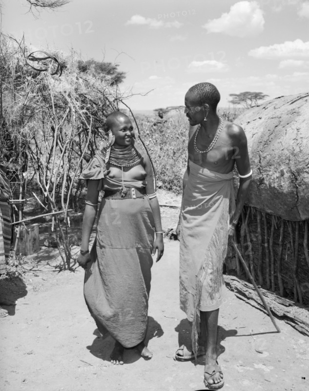 Lepuipui with a Samburu woman. A Samburu man identified as 'Lepuipui' chats to a young Samburu woman in a village. Both wear traditional dress: her's decorated with striking, ornate jewellery. Wamba, Kenya, 13 October 1956. Wamba, Rift Valley, Kenya, Eastern Africa, Africa.