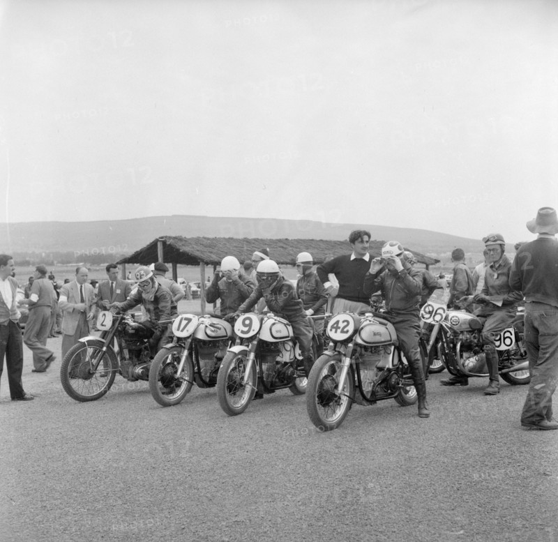 Nakuru motorcycle race. A group of riders sit astride their numbered motorcycles, adjusting their goggles at the start of a race. Nakuru, Kenya, 6 August 1956. Nakuru, Rift Valley, Kenya, Eastern Africa, Africa.