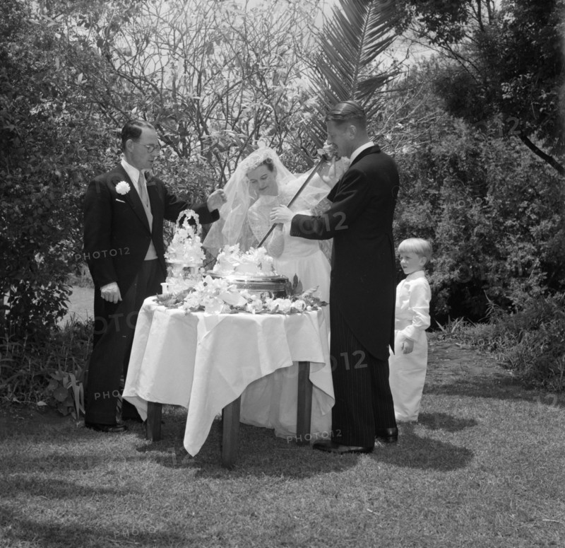 Cutting the cake with a ceremonial sword. The newlywed Williams and McLaughlin couple cut their wedding cake with a ceremonial sword. Kenya, 22 August 1956. Kenya, Eastern Africa, Africa.