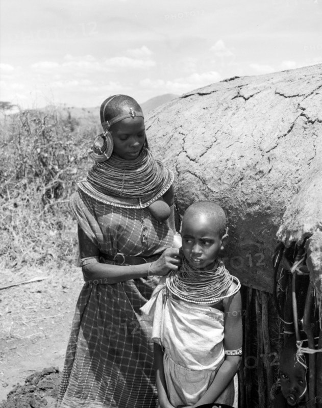 Samburu woman and child. A Samburu woman adjusts a child's necklace. She wears traditional dress and jewellery consisting of a heavily beaded necklace and striking, ornate earrings. Wamba, Kenya, 13 October 1956. Wamba, Rift Valley, Kenya, Eastern Africa, Africa.
