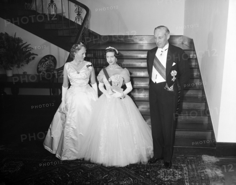 Princess Margaret with Sir Evelyn Baring. Dressed in evening gowns, long gloves and tiaras, Princess Margaret and Lady Mary descend the stairs to pose for the camera with the Governor of Kenya, Sir Evelyn Baring. Kenya, 19 October 1956. Kenya, Eastern Africa, Africa.