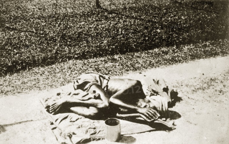 A India fakir in Ceylon. An Indian fakir lies hunched up with a begging bowl on a sack outside the sacred Dalada Maligawa or Temple of the Buddha's Tooth. Kandy, Ceylon (Sri Lanka), 27-31 January 1924. Kandy, Central (Sri Lanka), Sri Lanka, Southern Asia, Asia.
