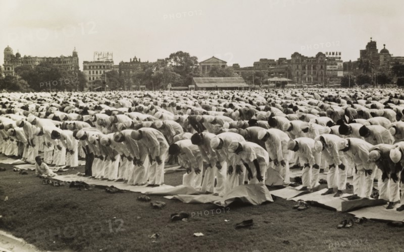Prayers during Eid. Hundreds of Muslim men, standing bare-foot on prayer mats, bow their upper bodies in prayer in during the Islamic festival of Eid. Calcutta (Kolkata), India, circa 1954. Kolkata, West Bengal, India, Southern Asia, Asia.