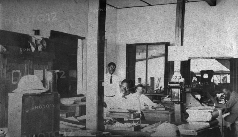 Tamlin in the office. Mr Alfred Tamlin sits in his office accompanied by three African employees. Western Africa, circa 1920., Western Africa, Africa.