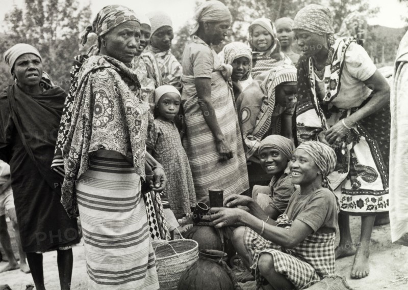 Women at a Tanganyikan market. Women laugh and chat as they examine goods at a local market. Tanganyika Territory (Tanzania), circa 1960. Tanzania, Eastern Africa, Africa.