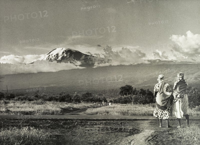 Kilimanjaro skyline. Two African women take in a view of Mount Kilimanjaro. Tanganyika Territory (Tanzania), circa 1960. Tanzania, Eastern Africa, Africa.