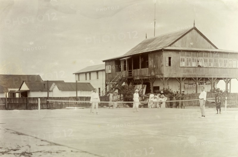 Mr. Tamlin plays tennis. Mr Alfred Tamlin (the European figure on the right) plays tennis with his colleagues. A group of Africans watch the game from the side of the court. Probably Accra, Gold Coast (Ghana), circa 1918. Ghana, Western Africa, Africa.