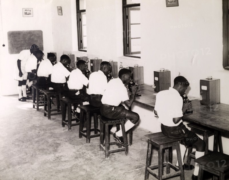 Tanganyikan students with microscopes. Official publicity shot for the Tanganyikan government. A group of young men in uniform operate microscopes during a college science lesson. Tanganyika Territory (Tanzania), circa 1950. Tanzania, Eastern Africa, Africa.