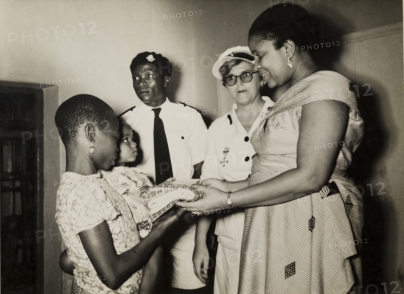 Staff meet patients at a British Red Cross Clinic. Staff meet patients at a Children's Welfare Clinic run by the British Red Cross, during a royal visit from Princess Mary, Countess of Harewood. The staff are identified left to right as: Mr F.O. Sholeye (Regional Secretary), Mrs E.C. Alderton (Regional Nursing Superintendant) and Mrs Mhamdi Azikiwe (Regional Director). Enugu, Anambra State, Nigeria, 16 November 1957., Enugu, Nigeria, Western Africa, Africa.