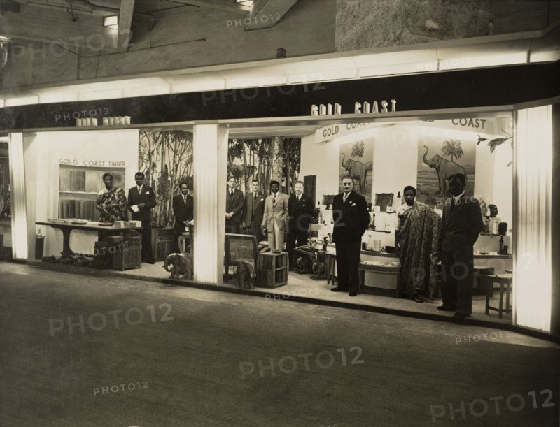 Gold Coast stand at British Industries Fair. An official photograph, taken for the Gold Coast Colonial Office, of the Gold Coast stand at the British Industries Fair. British and African men attend the stall, which displays a collection of African objects and an exhibit about Gold Coast timber. London, United Kingdom, 1950. London, London, City of, England (United Kingdom), Western Europe, Europe .