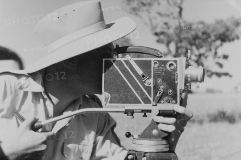 Filming for the Central African Film Unit. A European cameraman operates a movie camera on location at Goromonzi, during the shooting of a police film for the Central African Film Unit (CAFU). Goromonzi, Southern Rhodesia (Zimbabwe), May 1954. Goromonzi, Mashonaland East, Zimbabwe, Southern Africa, Africa.