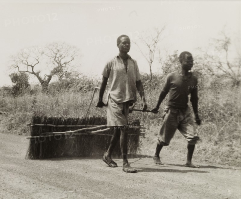 Smoothing corrugations in a road. Two men smooth over corrugations in a road by dragging a section of bound brushwood across its surface. Zomba, Nyasaland (Malawi), circa 1957., Zomba, Malawi, Southern Africa, Africa.