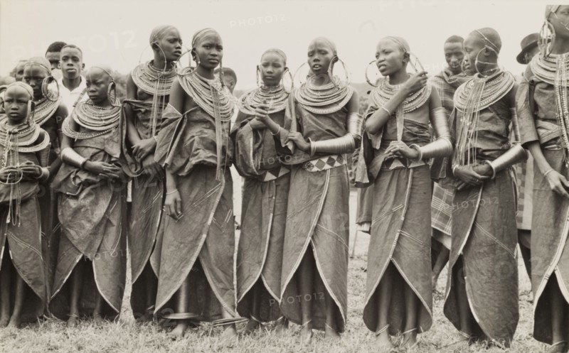 A group of Maasai women. A traditionally dressed group of young Maasai women stand in line. Their heads are shaven and they wear ornate jewellery including large hooped earrings, armlets and masses of beaded necklaces. Eastern Africa, circa 1955., Eastern Africa, Africa.