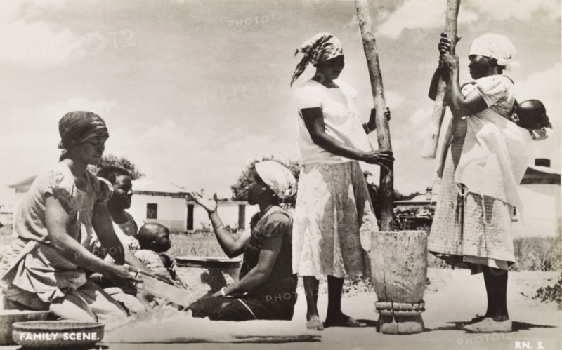 A domestic scene. Domestic scene showing a group of women working together outdoors in an African village. One woman separates grain with a sieve, whilst two others pound it using a large pestle and mortar. Southern Africa, circa 1950., Southern Africa, Africa.