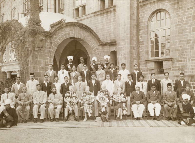 Government employees, India. Two British couples, adorned with garlands and bouquets of flowers, pose at the centre of a group portrait, surrounded by rows of Indian government workers. The British man to the left may be Mr Caffin, a one time District Officer of the Northern Province. India, circa 1945. India, Southern Asia, Asia.