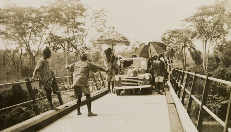 Opening of the Ishua to Ibillo bridge. People with parasols surround the first car to cross the Ishua to Ibillo road bridge at its official opening. Ondo, Nigeria, 5 January 1951., Ondo, Nigeria, Western Africa, Africa.