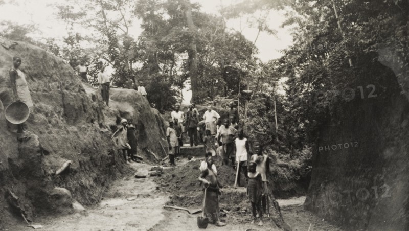 Widening the road from Imesi-Ile. A local labour force of men, women and children work to widen the road leading from Imesi-Ile. A European land owner identified as 'Kendal Robinson, the Resident', stands amongst the group. Osun, Nigeria, circa 1950., Osun, Nigeria, Western Africa, Africa.