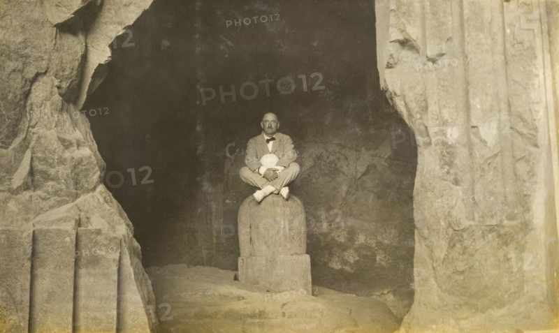 Inside the Elephanta Caves. A European man sits cross-legged, posing for the camera on a stone sculpture inside the Elephanta Caves. Elephanta Island, Maharashtra, India, circa 1920. Elephanta Island, Maharashtra, India, Southern Asia, Asia.