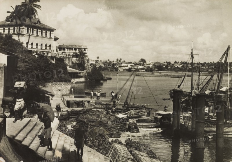 Mombasa Old Port, 1950. View across Mombasa's Old Port showing tradesmen unloading crates from small vessels docked nearby. Mombasa, Kenya, 1950. Mombasa, Coast, Kenya, Eastern Africa, Africa.
