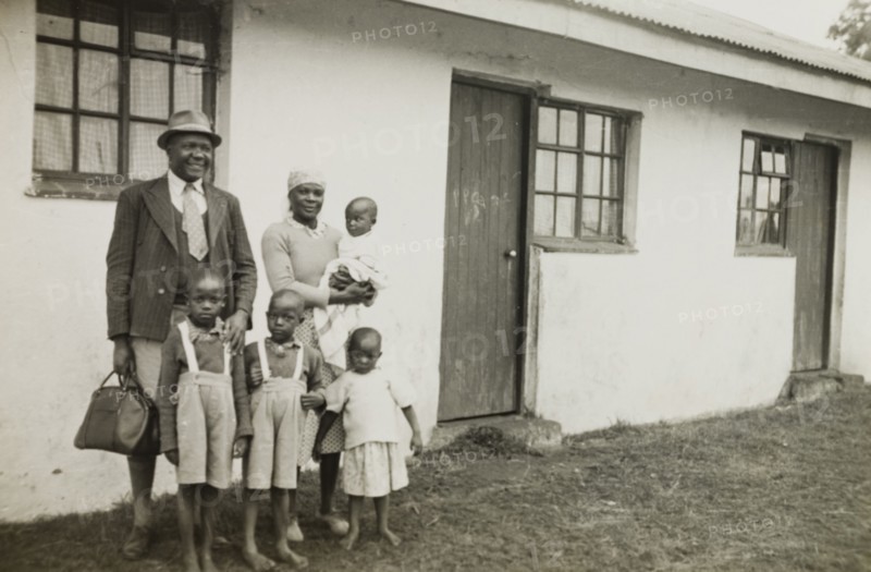 A theology student and his family, Kenya. A student of St. Paul's United Theological College in Limuru, stands with his wife and four children outside a single storey house, provided for him and his family by the college. The college was established by missionaries to train African ordinands for the priesthood and to educate their wives. Limuru, Kenya, circa 1956. Limuru, Central (Kenya), Kenya, Eastern Africa, Africa.