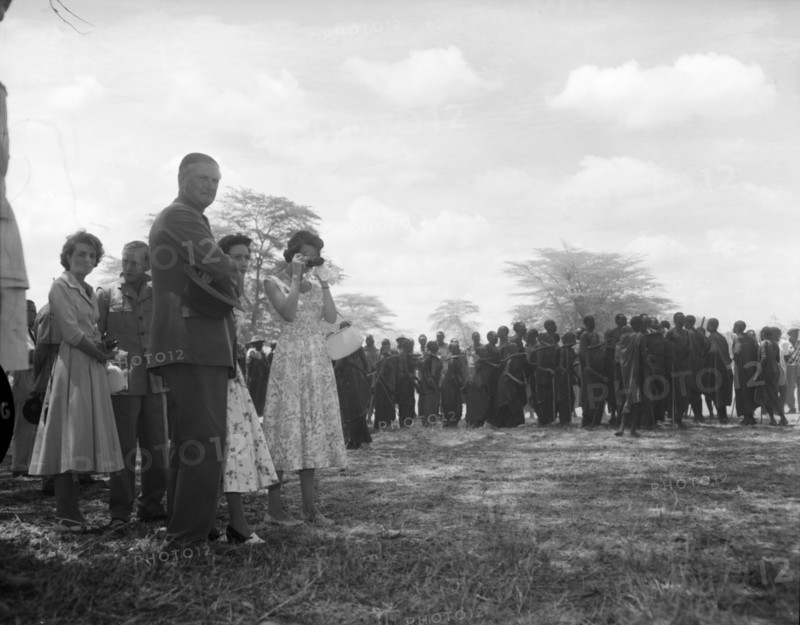 Princess Margaret watches a Maasai dance. Princess Margaret and her entourage watch from the sidelines as Maasai dancers wearing traditional dress prepare for a performance. Amboseli, Tanganyika Territory (Tanzania), 23 October 1956. Amboseli, Kilimanjaro, Tanzania, Eastern Africa, Africa.